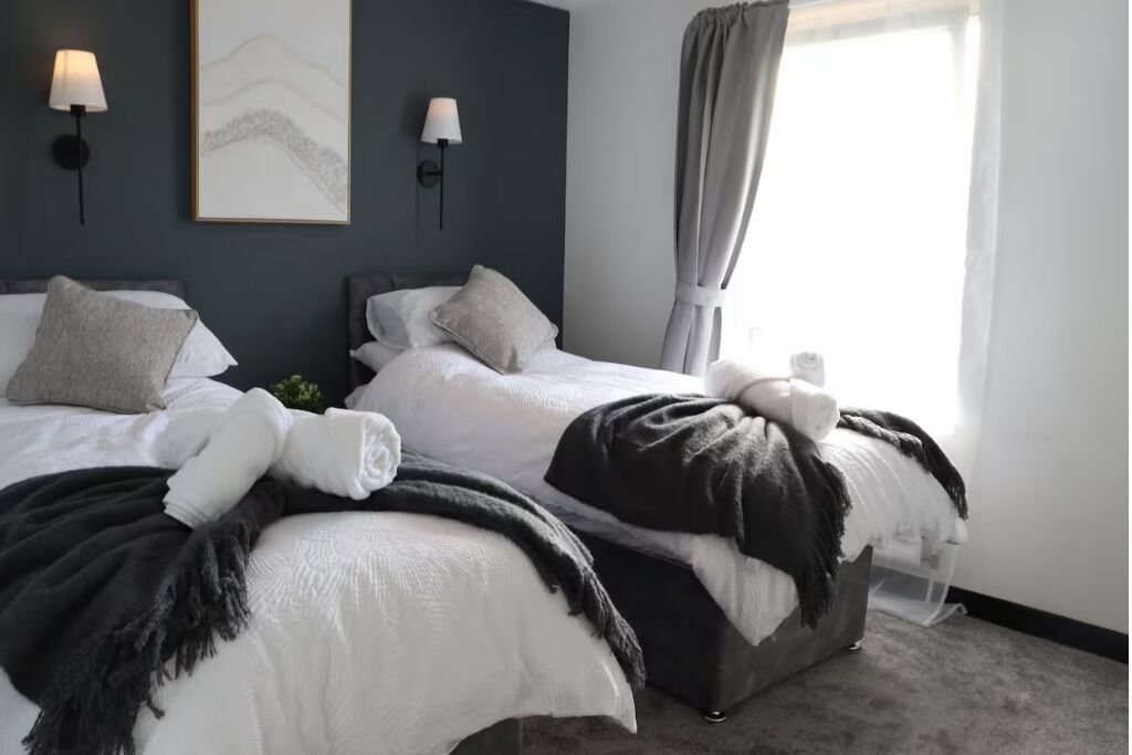 Een hotelkamer met twee bedden, een grijze gordijn, wandlampen en een lijstwerk.