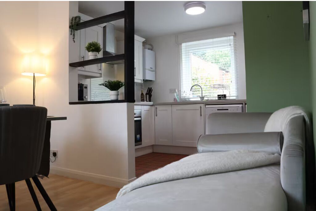 Una habitación compacta con cama, escritorio con silla, kitchenette y ventana con persianas.