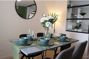 A dining table set with teal plates, bowls, and cutlery, a vase with white flowers, and a mirror on the wall.