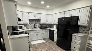 A modern kitchen with white cabinetry, a black refrigerator, and a tiled backsplash. - The Boyer House Beautiful Modern Farmhouse (Paducah)