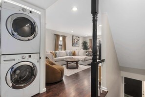 Une buanderie équipée de machines à laver et de sèche-linge superposés, un salon avec un canapé, une table basse et une cheminée.