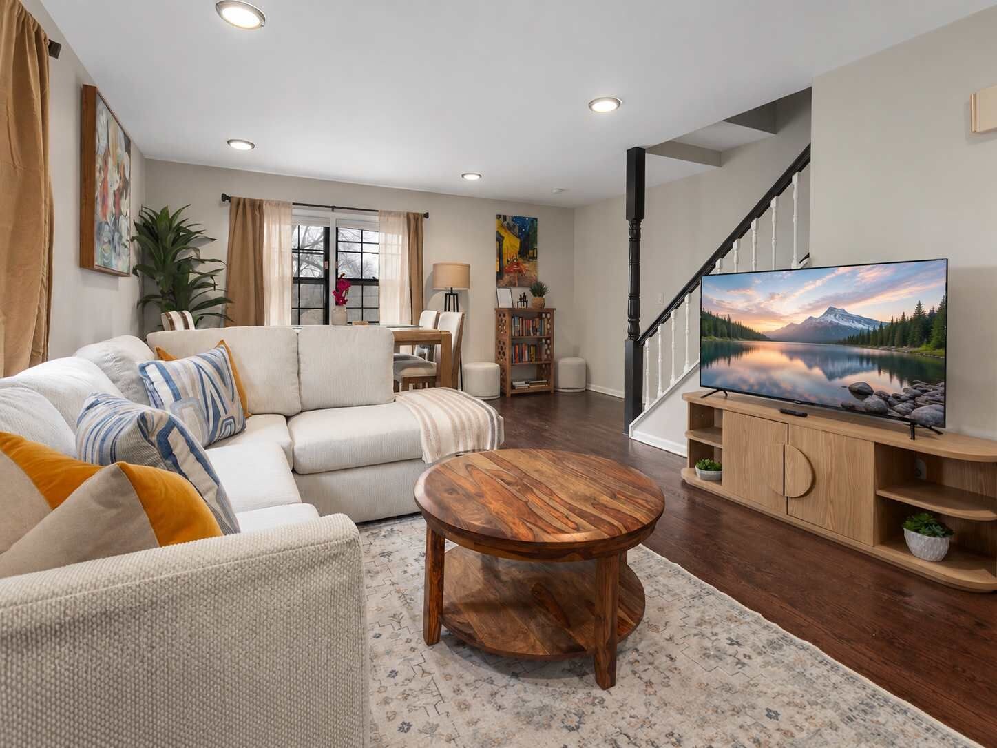 Ein Wohnzimmer mit einer Couch, Couchtisch und Fernseher. Eine Treppe mit Geländer ist ebenfalls vorhanden.