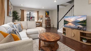 Ein Wohnzimmer mit einer Couch, Couchtisch und Fernseher. Eine Treppe mit Geländer ist ebenfalls vorhanden.