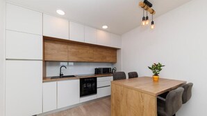 Una cocina moderna con armarios blancos, encimera de madera, horno empotrado y un comedor con mesa y sillas de madera.