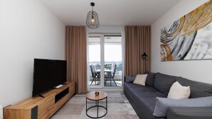 Una sala de estar moderna con un televisor de pantalla plana, un sofá gris, un mueble de entretenimiento de madera, una mesa de centro redonda y un cuadro abstracto grande en la pared.