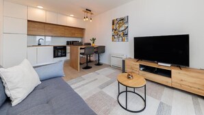 Un espacio de estar moderno con sofá, televisión, cocina y comedor.