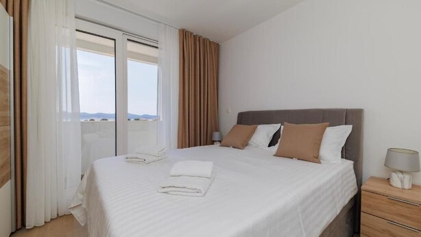 Habitación de hotel con una cama grande, una mesita de noche, una lámpara y vistas a través de una ventana.