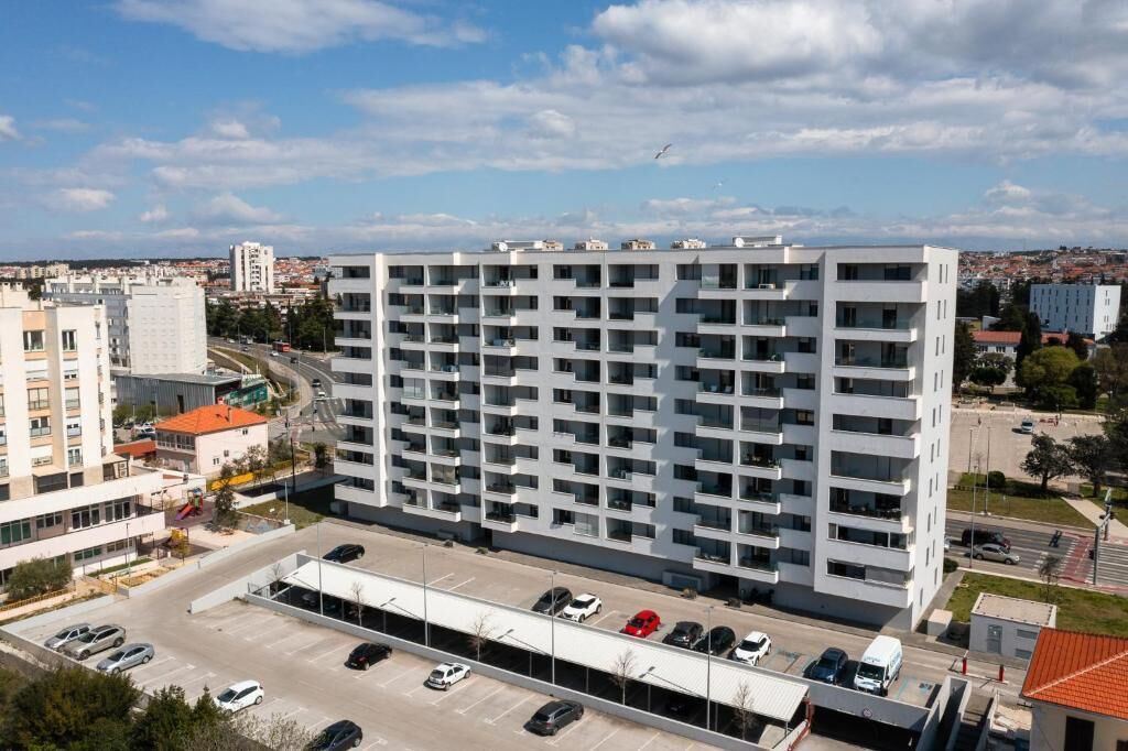Un immeuble à plusieurs étages, avec un parking à l’avant, entouré d’autres bâtiments.