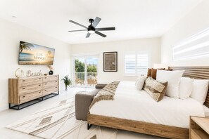 Ein Schlafzimmer mit einem Bett, einem Deckenventilator, einem Fernseher, einem Schminktisch und einem Balkon.