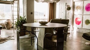 A modern dining area with a round table, chairs, a chandelier, and a large window with a view.