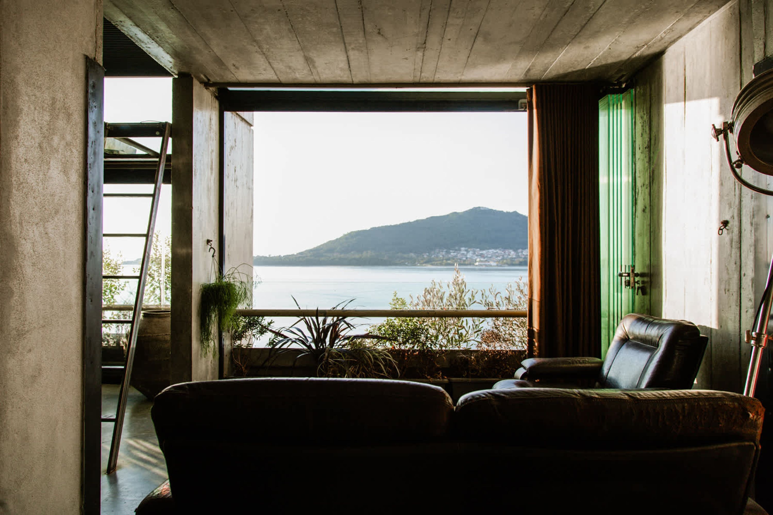 A room with a view of a body of water and a mountain, a chair, a ladder, and a green door.