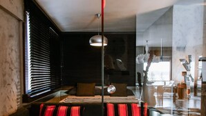 A modern living room with a sofa, a rug, and a dining area visible through a glass partition.