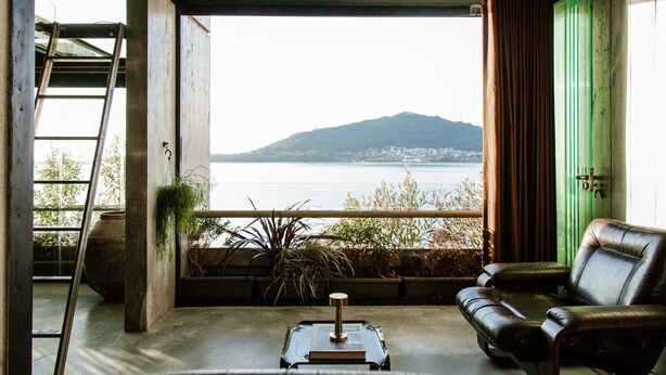 A room with a view of a body of water and a mountain, a ladder, a green door, and a leather sofa.