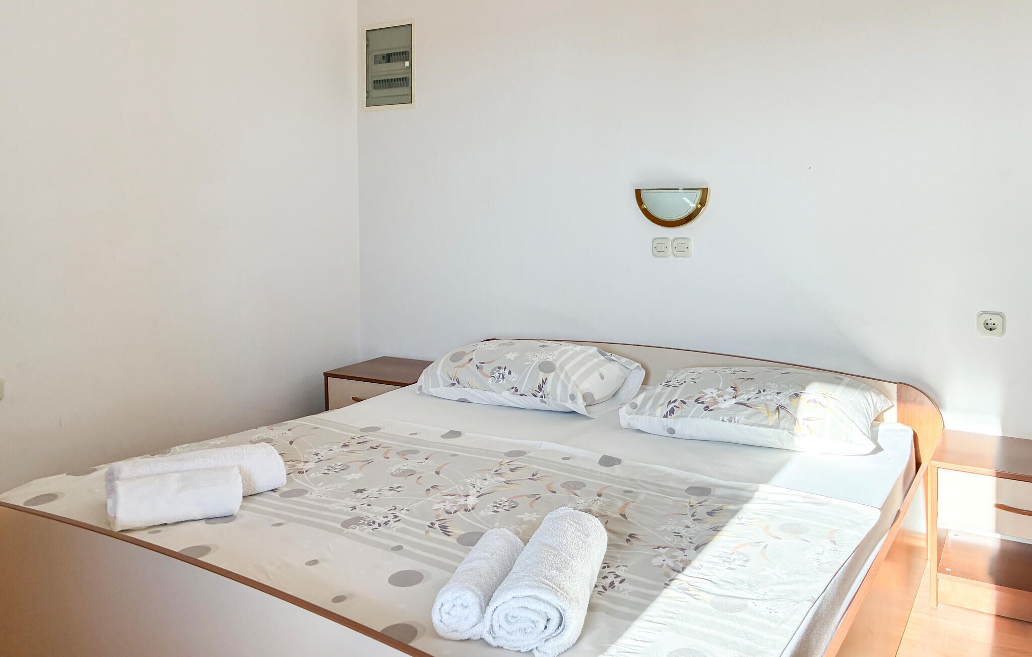 A neatly made bed with a floral-patterned bedspread and two rolled towels.