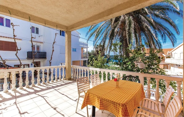 A balcony with a checkered table and chairs, overlooking a residential area and palm trees.