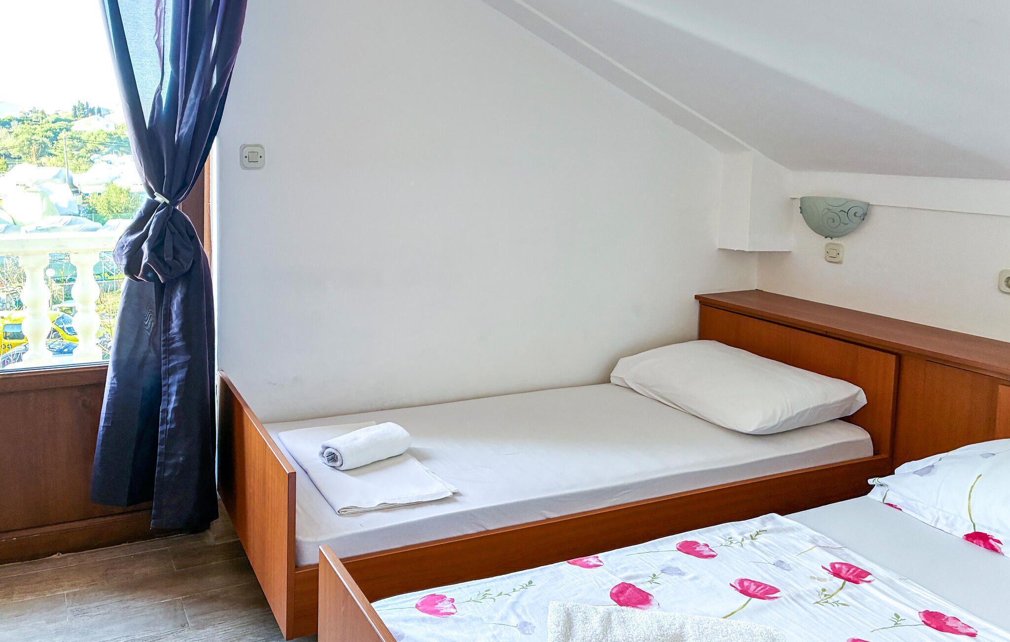 Une petite chambre avec un lit simple, une tête de lit en bois, une table de chevet et une fenêtre avec des rideaux.