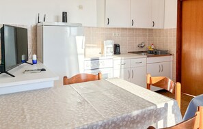 Eine kleine Küche mit Kühlschrank, Herd und Spüle. Ein Esstisch mit Stühlen steht bereit.
