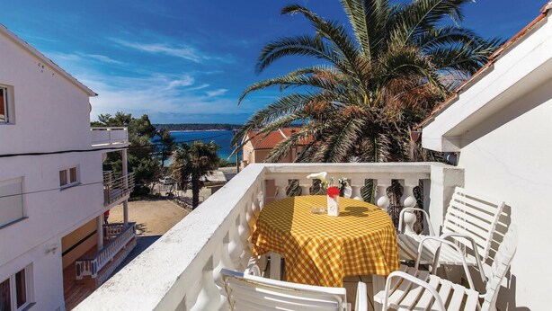 Un balcon avec une nappe à carreaux, des chaises blanches et une vue sur la mer et les bâtiments.