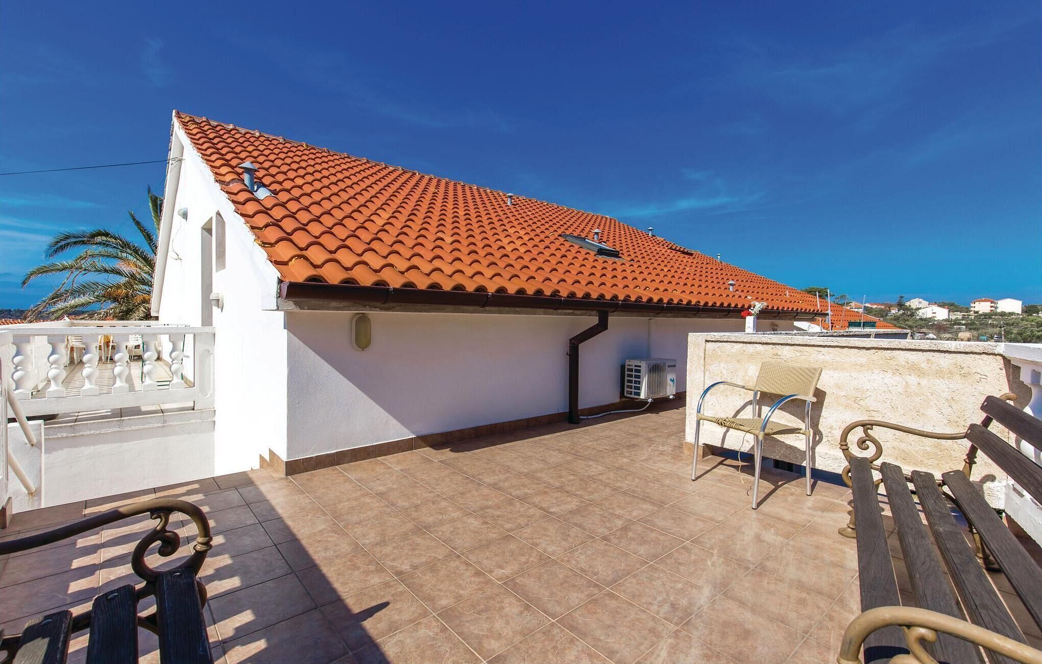 A rooftop terrace with a red-tiled roof, a white wall, and a view of the surrounding landscape.