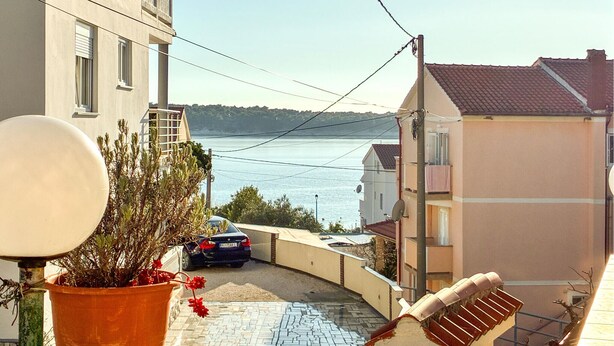 Eine enge Straße mit Blick auf das Meer, ein geparktes Auto und ein Gebäude mit einem Balkon.