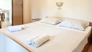 Ein ordentlich bezogenes Bett mit weißen Leinen und aufgerollten Handtüchern, ein Nachttisch und eine Wandleuchte.