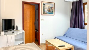Ein Zimmer mit Fernseher, einem Gemälde, einer Couch, einem Tisch und einem Stuhl.