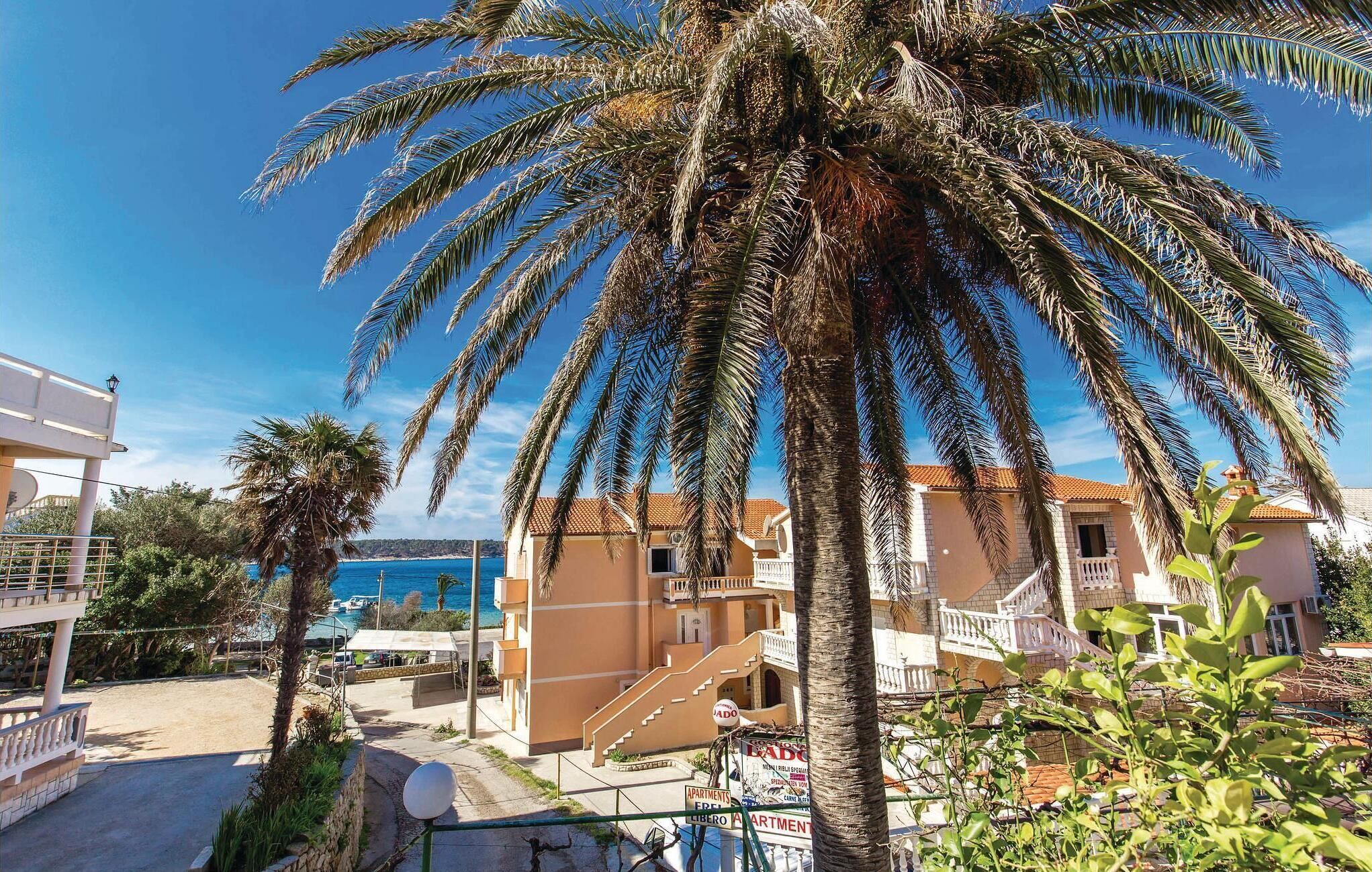 A coastal building complex with multiple balconies, a clear view of the sea, and a palm tree in the foreground.