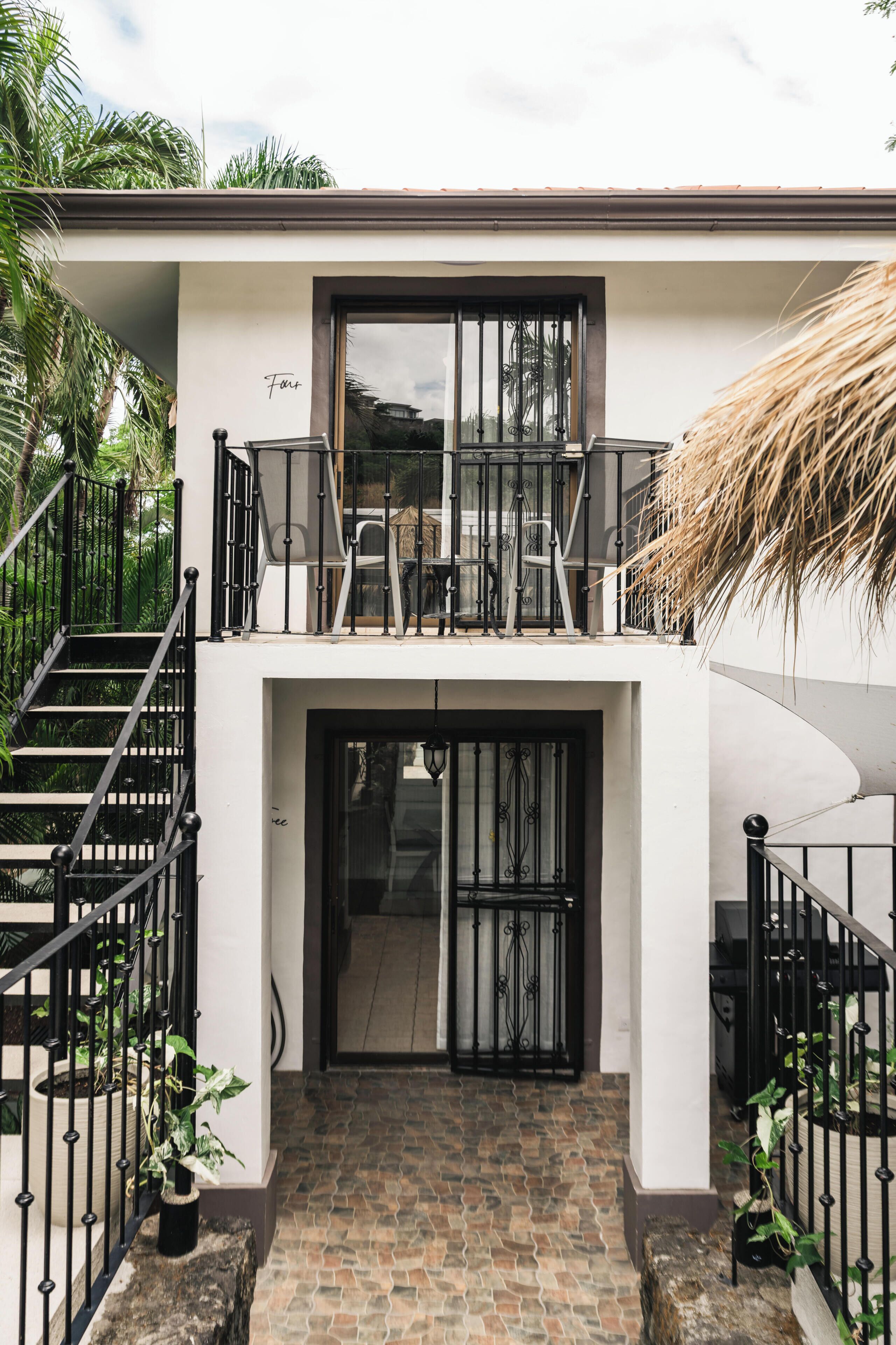 A modern two-story building with a staircase, a balcony with outdoor furniture, and potted plants.