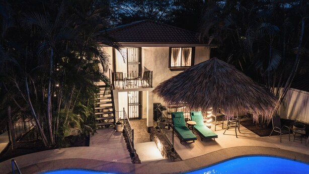 A two-story house with a swimming pool, a thatched-roof outdoor seating area, and lush tropical vegetation. - King Suite I Full Kitchen I Pool, Spa & Balcony I Near Beach I Suite Four (Del Coco Beach)