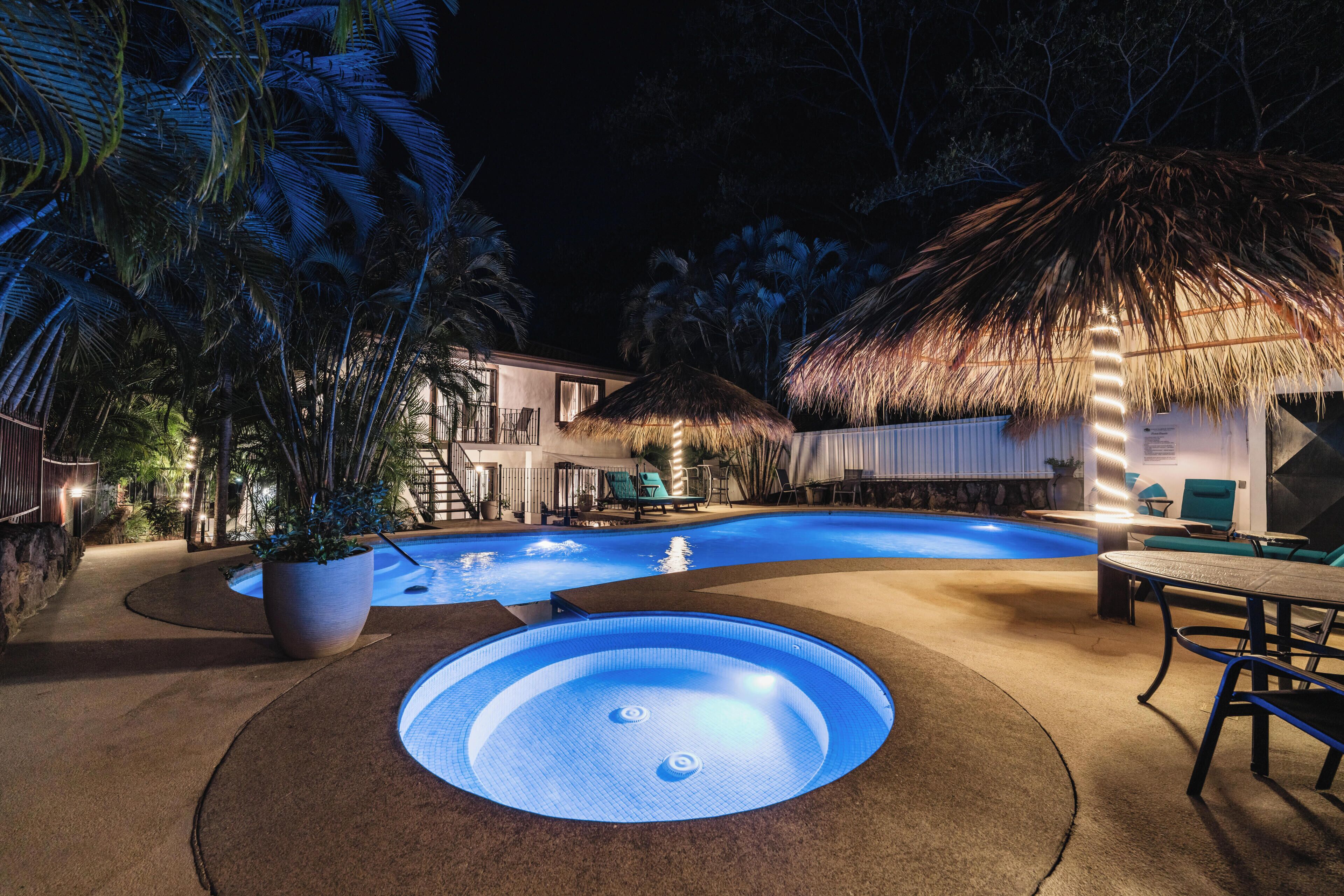 Uma piscina com hidromassagem, espreguiçadeiras e uma estrutura de telhado de palha.