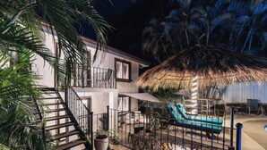 A modern house with a staircase, a pool area with lounge chairs, and a thatched roof. - King Suite I Full Kitchen I Pool, Spa & Balcony I Near Beach I Suite Four (Del Coco Beach)