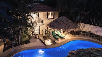 A two-story house with a swimming pool, a thatched-roof outdoor area, and a staircase leading to the upper floor.