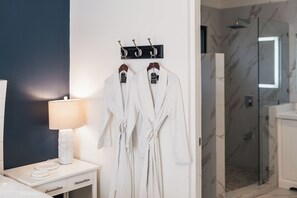 A bathroom with a white bathtub, a glass shower enclosure, and a robe rack with two robes. - King Suite I Ensuite I Kitchenette | Pool, Spa & Patio I Near Beach I Suite One (Del Coco Beach)