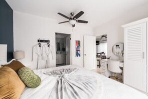 A bedroom with a bed, a ceiling fan, a wardrobe, a desk, and a bathroom visible through an open door. - King Suite I Ensuite I Kitchenette | Pool, Spa & Patio I Near Beach I Suite One (Del Coco Beach)