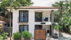 A two-story building with a balcony, potted plants, and a stone wall.