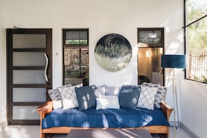 Una habitación con sofá de madera, un espejo redondo y una lámpara azul.