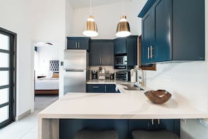 A modern kitchen with dark cabinets, stainless steel appliances, and pendant lighting.