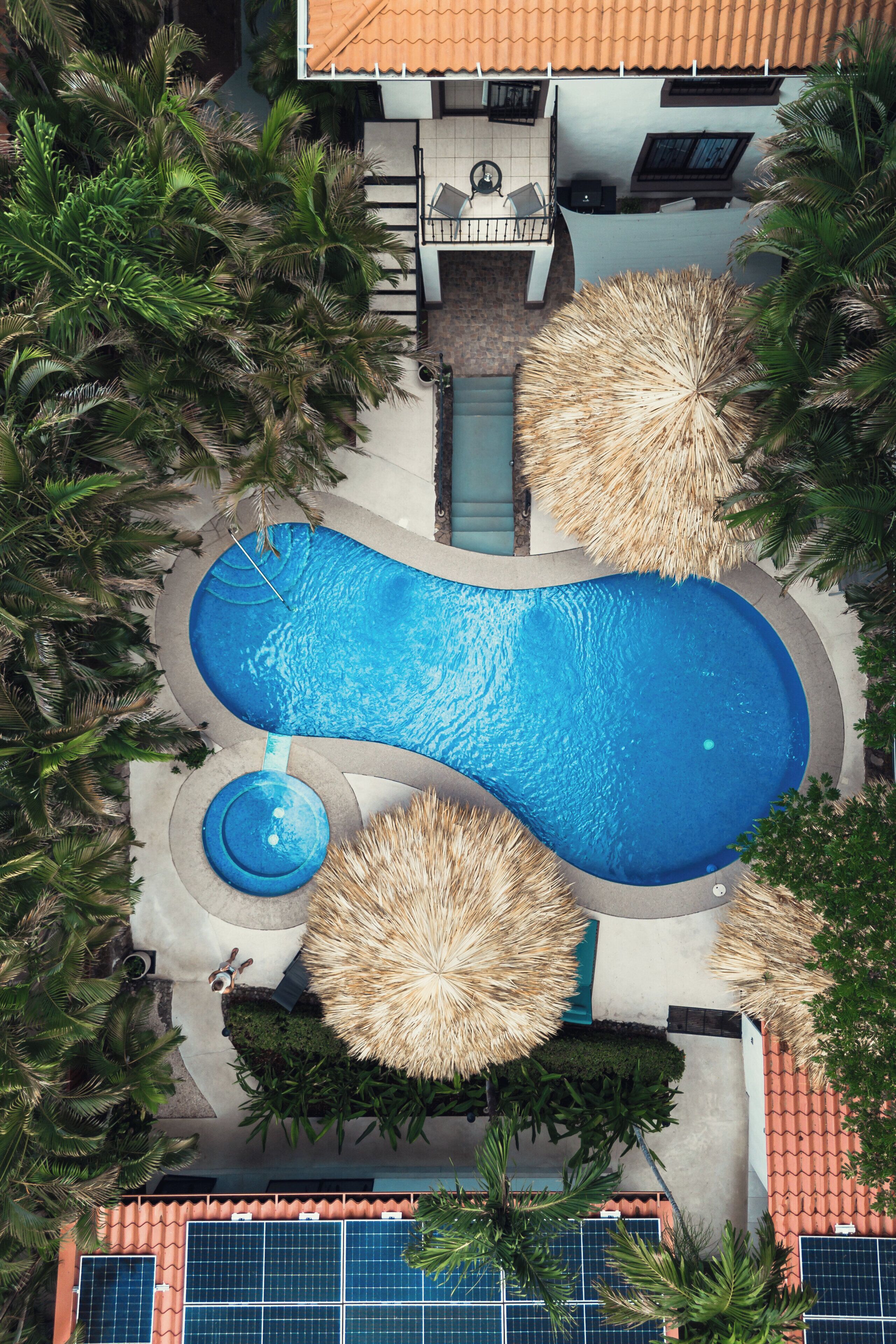 Vista aerea di una piscina circondata da palme e da un edificio con tetto in tegole.