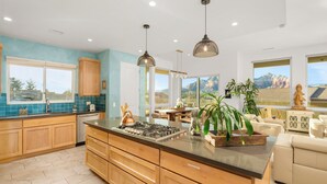 Een moderne keuken met houten kastjes, een centraal eiland, hanglampen en grote ramen met uitzicht op de omgeving.