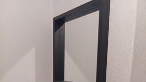 A bathroom with white tiled walls, a marble accent, a black-framed mirror, and a toilet paper holder.