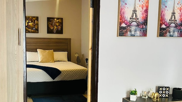 A hotel room with a bed, a wooden wardrobe, and two paintings of the Eiffel Tower.
