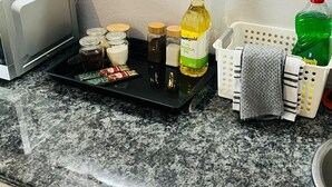 A kitchen counter with a microwave, jars, a bottle of oil, a dish soap bottle, and a basket with towels.