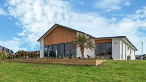 Un bâtiment moderne doté de grandes fenêtres, d’un toit en pente et d’un jardin paysager à l’avant.