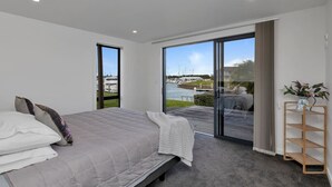 Une chambre avec un lit, une vue sur un port de plaisance, une porte-fenêtre coulissante et une étagère en bois ornée d’une plante.