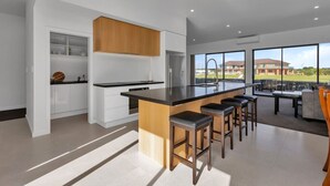 Une cuisine moderne dotée d’un îlot central, de tabourets de bar et offrant une vue sur un quartier résidentiel.