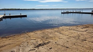 Tyyni järvi, jonka rannalla on kaksi laituria, jotka ulottuvat veteen. Järveä ympäröi hiekkaranta.