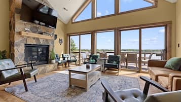 A spacious living room with a stone fireplace, comfortable seating, and large windows offering a view of the outdoors.