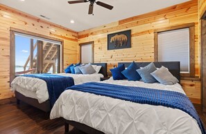 A double bedroom with two beds, wooden walls, a ceiling fan, and a large window. - Lake Front | Pontoon | Arcade | Beach | Hot Tub (New Lisbon)