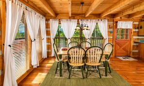 A wooden cabin with a dining table, chairs, and a hanging light fixture. - Hard to Leave - Stunning Mountain Views, Pool Table, Games, Hot Tub! (Sevierville)