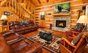 A log cabin interior with a leather sofa, a stone fireplace, and a television mounted above it. - Hard to Leave - Stunning Mountain Views, Pool Table, Games, Hot Tub! (Sevierville)